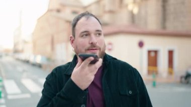 Genç ve cüsseli bir adam gülümsüyor. Akıllı telefondan konuşuyor.