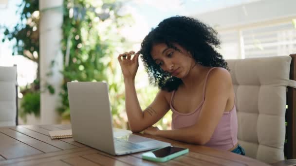 若いですヒスパニック系の女性使用してノートパソコンの上に座っているテーブルの上に深刻な表現でホームテラス — ストック動画