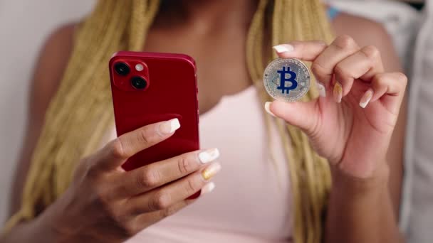 Αφροαμερικανή Γυναίκα Που Χρησιμοποιεί Smartphone Κρατώντας Bitcoin Στο Σπίτι — Αρχείο Βίντεο