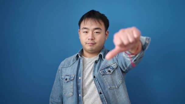 Молодой Китаец Делает Негативный Жест Опущенными Пальцами Изолированном Синем Фоне — стоковое видео