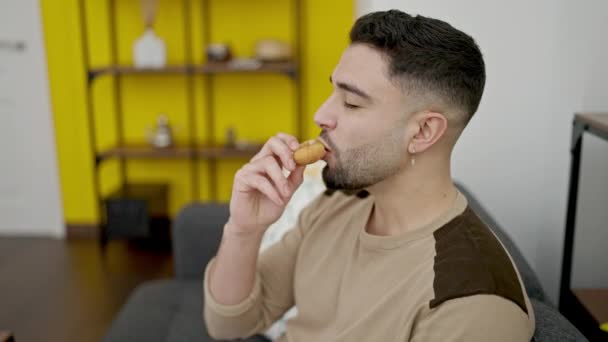 Jovem Árabe Homem Comer Donut Sentado Sofá Casa — Vídeo de Stock