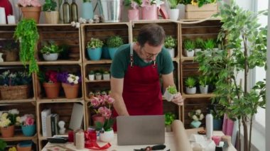 Çiçekçide dizüstü bilgisayar kullanan orta yaşlı bir çiçekçi.