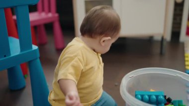 Adorable hispanic baby playing with construction blocks sitting on floor at kindergarten