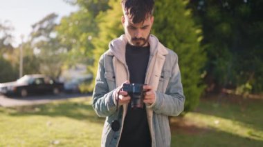 Young hispanic man standing with serious expression using camera at park