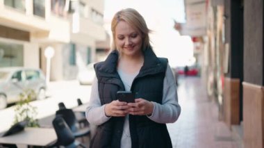 Sokakta akıllı telefon kullanan, kendine güvenen genç sarışın kadın.