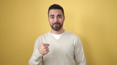Genç İspanyol adam, izole edilmiş sarı arka planda negatif jest yapıyor.