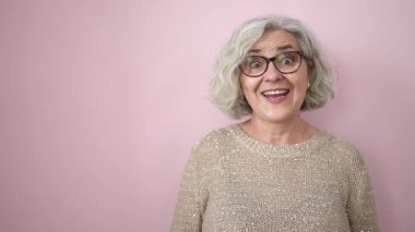 Middle age woman with grey hair standing with surprise expression pointing to the side over isolated pink background