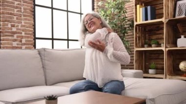 Middle age grey-haired woman suffering for neck pain at home