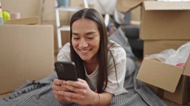 Genç, güzel, İspanyol bir kadın yeni evinde yerde yatarken akıllı telefon kullanıyor.
