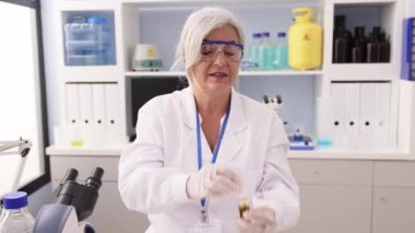 Orta yaşlı, gri saçlı, bilim adamı üniforması giyen, laboratuarda çalışan pipeti kullanan bir kadın.