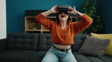 Young redhead woman playing video game using virtual reality glasses at home
