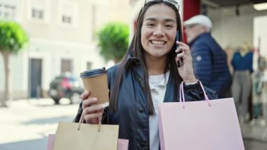 Güzel İspanyol bir kadın akıllı telefondan konuşuyor. Elinde alışveriş poşetleri ve sokakta kahve var.