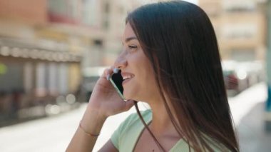 Genç, güzel, İspanyol bir kadın gülümsüyor ve caddede akıllı telefondan konuşuyor.