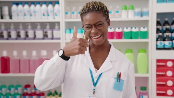 アフリカ系アメリカ人女性薬剤師笑顔自信を持って行いますOkジェスチャーとともに親指アップで薬局 — ストック動画