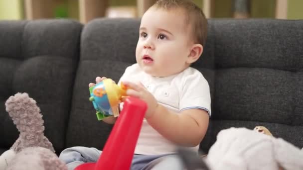 愛らしい幼児Bittingプラスチックおもちゃ座っています上のソファにホーム — ストック動画