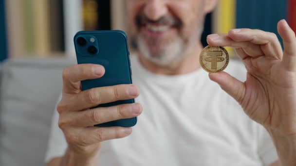 Чоловік Середнього Віку Тримає Криптовалюту Використанням Смартфона Вдома — стокове відео