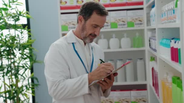 中年男子药剂师在药房的文件上写字 — 图库视频影像