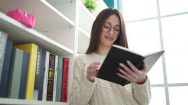 Young beautiful hispanic woman standing reading book at library university