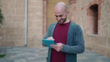 Young bald man smiling confident using touchpad at street