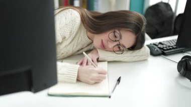Young beautiful hispanic woman student tired writing on notebook at library university