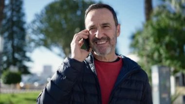 Middle age man smiling confident talking on smartphone at park