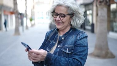 Middle age woman with grey hair using smartphone at street