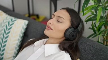 Genç, güzel İspanyol kadın evdeki kanepede rahatça müzik dinliyor.