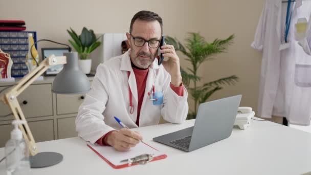 Чоловік Середнього Віку Лікар Розмовляє Смартфоні Пишучи Медичний Звіт Клініці — стокове відео