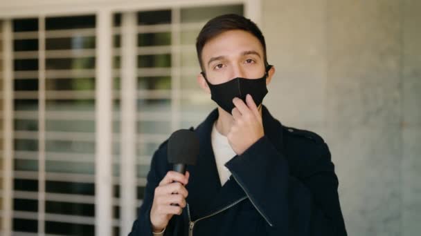 若いですヒスパニック男記者身に着けていますCovid保護マスク作業でマイクを使用してストリート — ストック動画