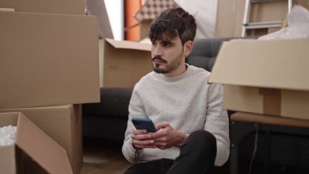 Jonge Spaanse Man Met Smartphone Zittend Vloer Een Nieuw Huis — Stockvideo