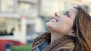 Young beautiful hispanic woman smiling confident looking to the sky at street