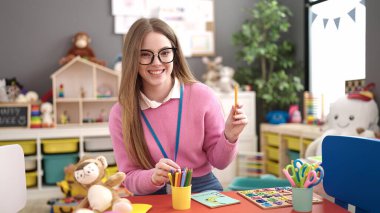 Young blonde woman working as teacher teaching color at kindergarten