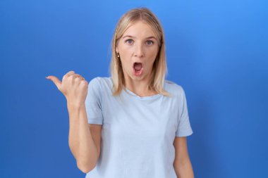 Gündelik mavi tişört giyen genç beyaz kadın elini yana uzatarak şaşırdı, ağzı açık hayret içinde kaldı.. 