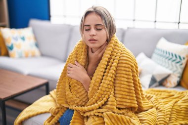 Evdeki kanepede oturan genç sarışın kadın baş ağrısı çekiyor.