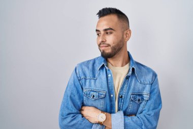 Tecrit edilmiş arka planda duran genç İspanyol adam kollarını kavuşturmuş, ikna olmuş ve kendinden emin bir şekilde yana bakıyor. 