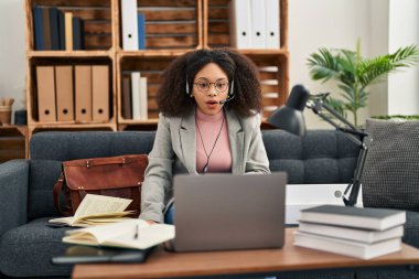 Genç Afro-Amerikalı kadın, danışma ofisinde çevrimiçi seans yapıyor. Şaşırmak ve şaşırmak için ağzı açık kalmış, inançsız. 