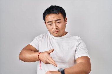 Beyaz arka planda dikilen genç Çinli adam zamanı, sabırsızlığı ve gecikmeyi izlemek için acele ediyor. 