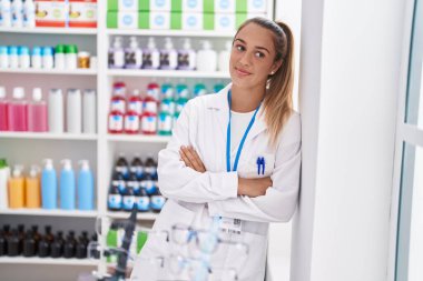 Young beautiful hispanic woman pharmacist smiling confident standing with arms crossed gesture at pharmacy