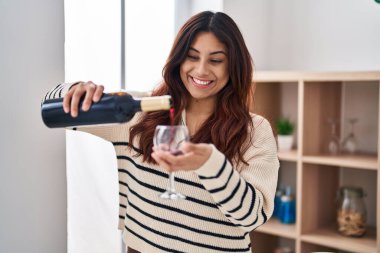 Young hispanic woman smiling confident pouring wine on glass at home