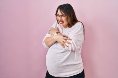 Hamile kadın pembe arka planda duruyor. Yüzünde üzgün ve şok ifadesiyle kış soğuğu için titriyor ve donuyor. 