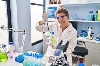 Laboratuvarda pipet kullanan bilim adamı üniforması giyen genç sarışın kadın.