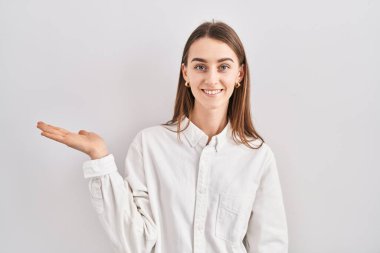 Kafkasyalı genç bir kadın izole edilmiş arka planda duruyor. Gülümsüyor, mutlu bir şekilde sunuyor ve avuç içiyle kameraya bakıyor.. 