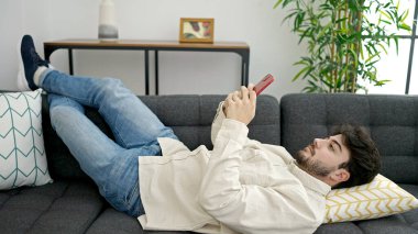 Evdeki kanepede uzanmış akıllı telefon kullanan genç bir İspanyol.