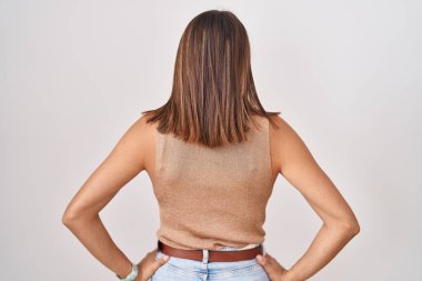 Beyaz arka planda duran Latin kökenli genç bir kadın kolları vücudunda geriye doğru bakıyor. 