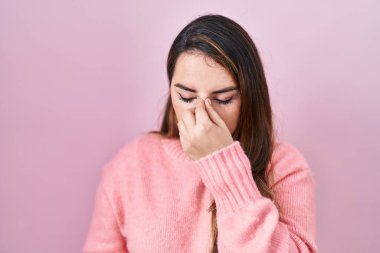 Pembe arka planda duran genç İspanyol kadın yorgun burnu ve gözleri ovuşturup yorgun ve baş ağrısı çekiyor. Stres ve hüsran kavramı. 