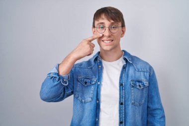 Beyaz, sarışın, gözlüklü, el parmağı ve burnuyla işaret eden neşeli gülümseyen adam. güzellik konsepti 