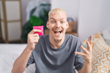 Elinde prezervatif tutan genç beyaz adam zaferi mutlu bir gülümseme ve ellerini kaldırarak kutluyor. 