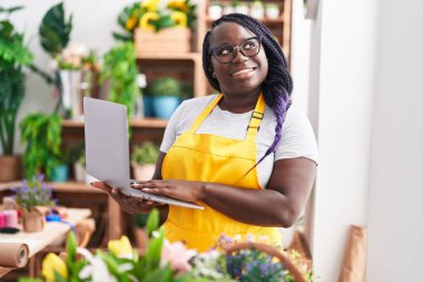 Çiçekçiye dizüstü bilgisayar kullanarak gülümseyen Afrikalı Amerikalı kadın.