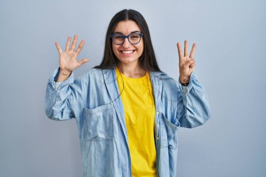 Mavi arka planda dikilen genç İspanyol kadın sekiz numaralı parmaklarını gösterip işaret ederken kendinden emin ve mutlu gülümsüyor.. 