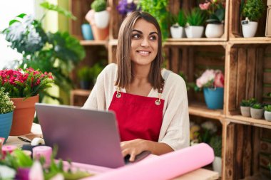 Young beautiful hispanic woman florist smiling confident using laptop at flower shop